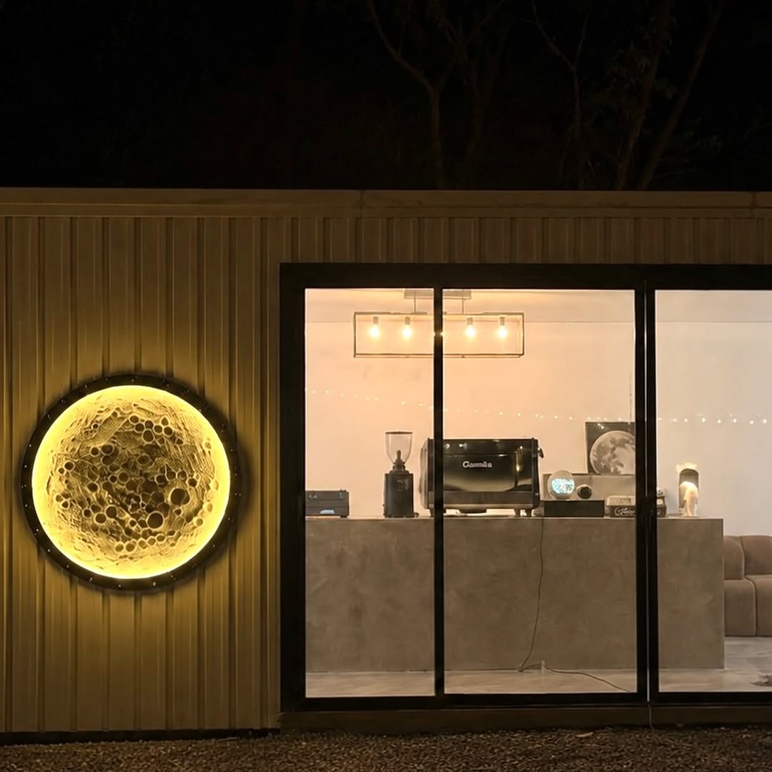 Moon Coffee 2.0 exterior at night — the glowing moon wall sculpture beside the glass-fronted espresso bar