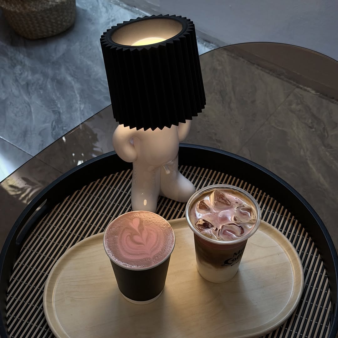 Moon Coffee drinks on a wooden serving tray — a hot pink latte with latte art and an iced coffee beside a lamp figurine