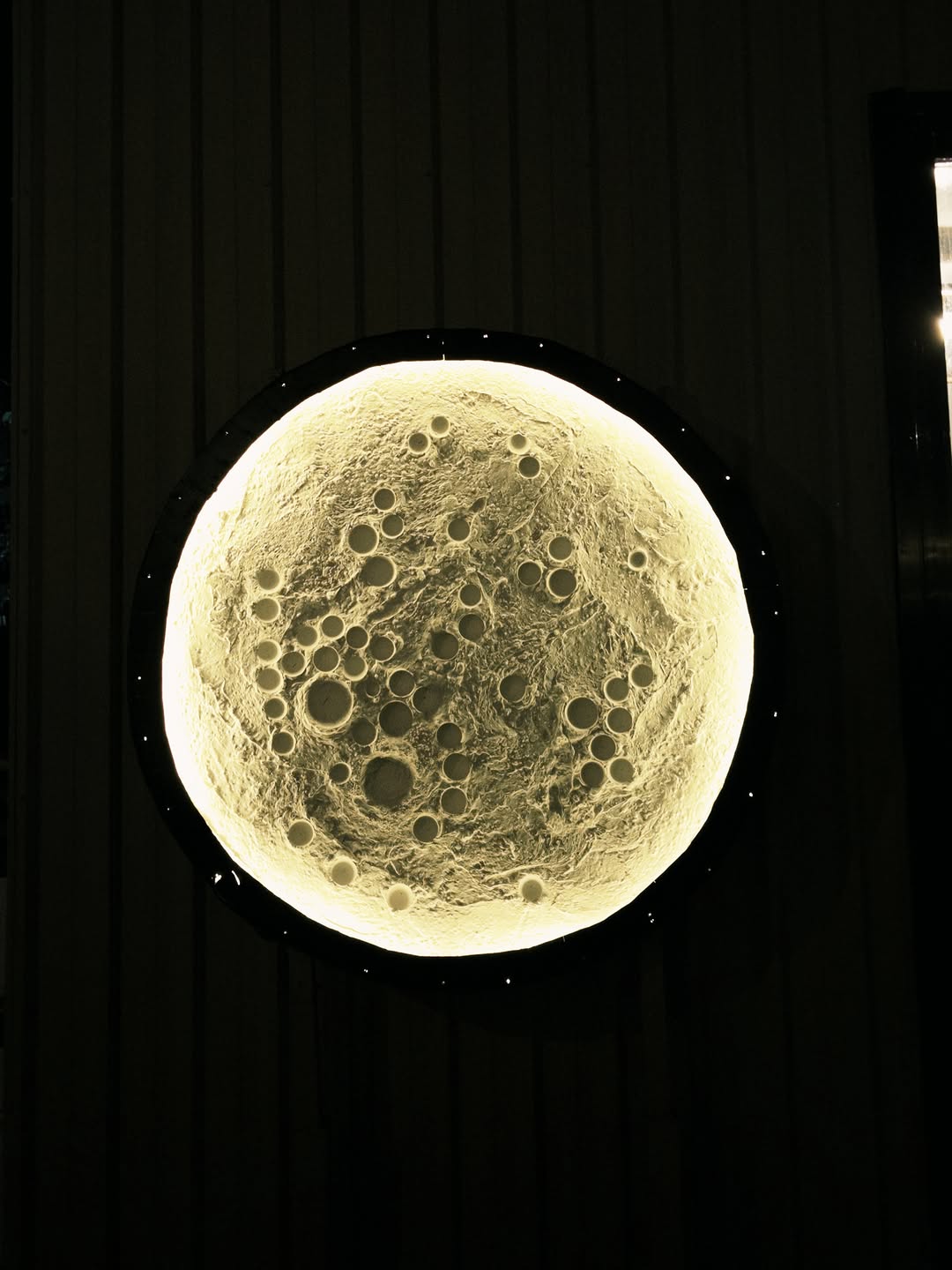 Moon Coffee's full moon wall lamp — a large illuminated moon sculpture mounted on the corrugated metal exterior