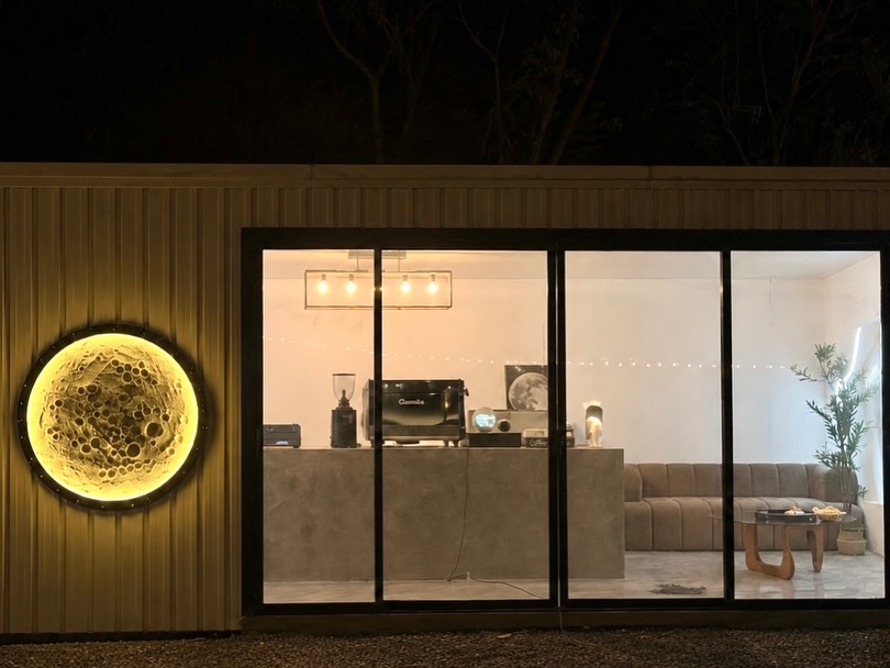 Moon Coffee 2.0 full exterior view at night — moon lamp, espresso bar, velvet sofa, and olive tree visible inside